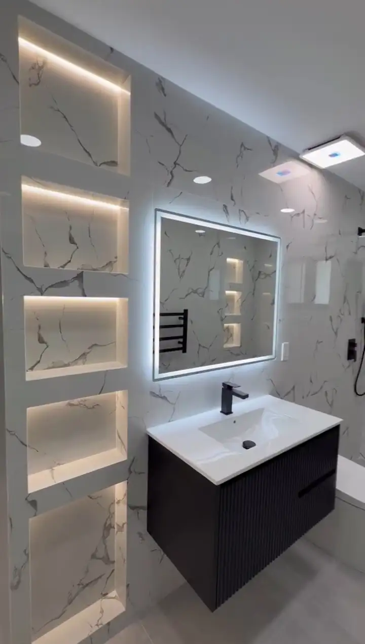Işıklı niş, aydınlatmalı ayna ve siyah dolaplı lavabo